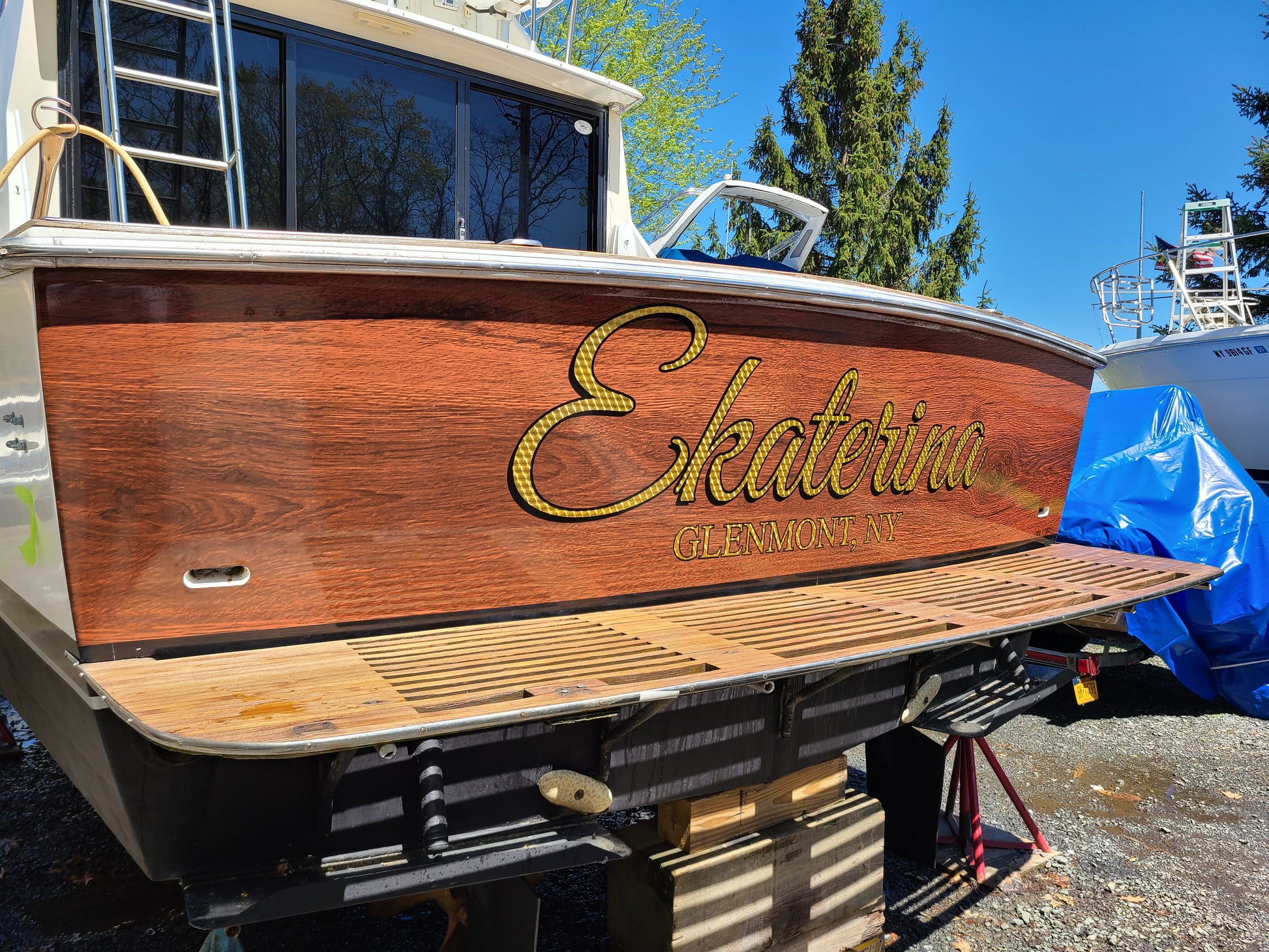 Teak wood boat wrap installed on transom.  Gold leaf vinyl lettering installed over vinyl wrap for boat name and port of call.  Boat signs.